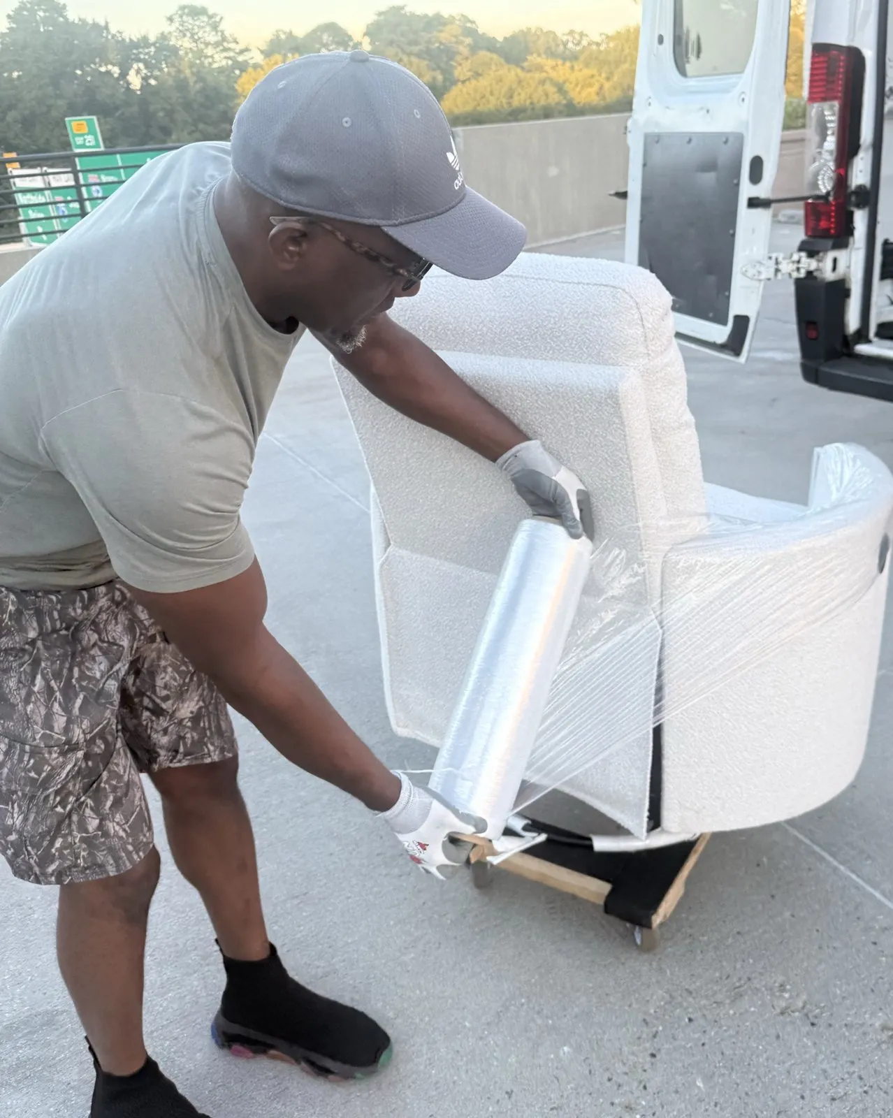 Jack shrink-wrapping a white swivel armchair on a dolly next to the van.